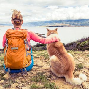 Woman hiker looking at sea with akita inu dog on seaside trail. Recreation and healthy lifestyle outdoors in summer mountains and sea nature. Beautiful inspirational landscape, trekking and activity.